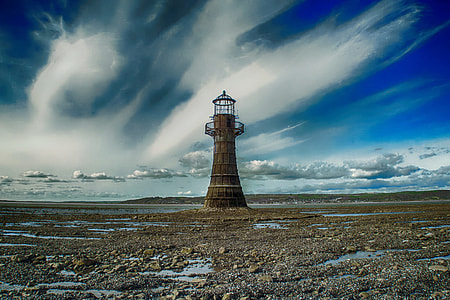 time lapse photography of brown lighthouse underneath blue cloudy skies thumbnail
