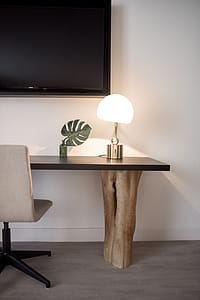 Stainless Steel Base White Shade Table Lamp on Brown Wooden Desk Near White Painted Wall With Wall Mounted Flat Screen T V thumbnail