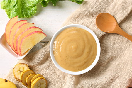 slice of apple fruit and banana fruit near bowl of sauce and wooden spoon thumbnail