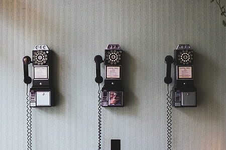 three rotary telephones on white wall thumbnail