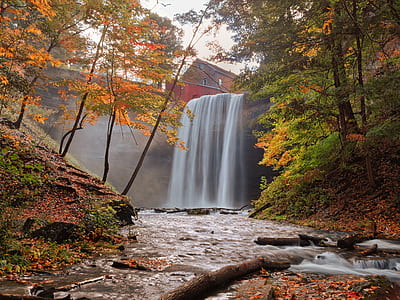 landscape photo of waterfalls flowing between tree-covered hills with view of orange and red house thumbnail