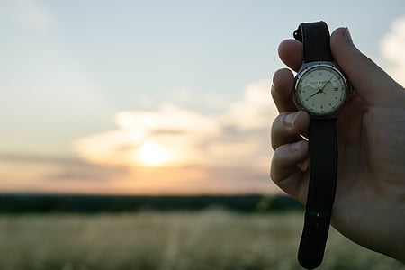 person holding round silver-colored analog watch outdoors thumbnail