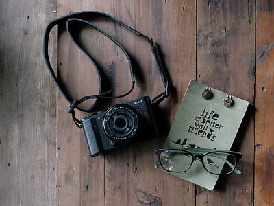 black SLR camera near black reading glasses on brown wooden surface thumbnail