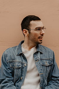 man wearing blue denim button-up jacket beside the wall thumbnail
