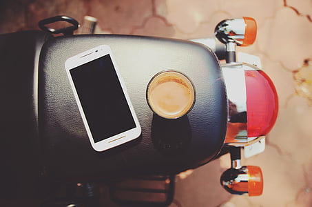 white Android smartphone beside black mug on top of black motorcycle seat thumbnail
