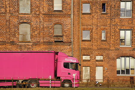pink freight truck near brown concrete building during daytime thumbnail