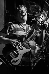 grayscale photography of man playing guitar while singing thumbnail