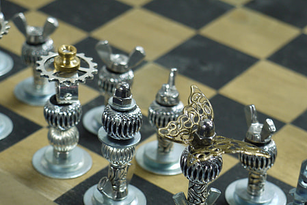 silver-colored gear chess pieces on beige and black board thumbnail