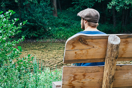 man sitting on the bench near body of water surrounded with trees thumbnail