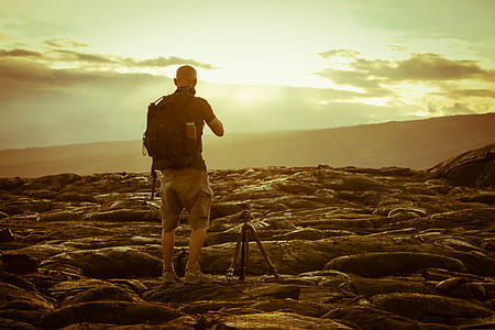 Man Beside Tripod on Rocks during Golden Hour thumbnail