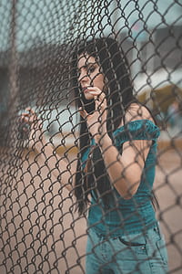 shallow focus photography of woman in green off-shoulder top holding black steel cyclone fence thumbnail