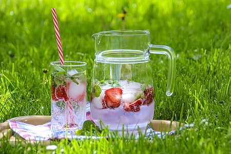 fruit juice in clear glass pitcher with drinking glass on green grass thumbnail