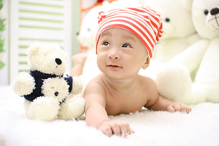 Smiling Toddler Wearing Orange and White Knit Cap Beside Black and White Bear Plush Toy thumbnail