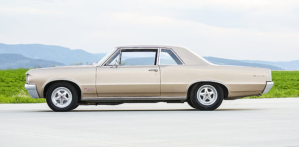 classic beige coupe parked on concrete pavement thumbnail