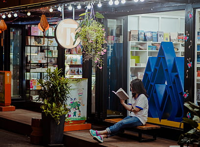 Woman Sitting Down On Bench And Reading Infront of Store thumbnail