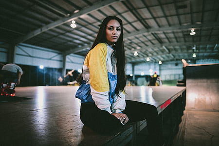 woman in white, blue, and yellow jacket sitting on gray platform thumbnail