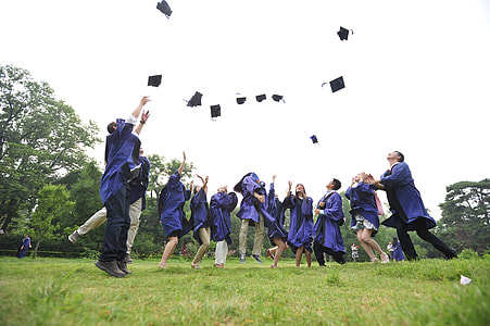newly graduates on green grass field wearing purple toga throwing their hats on air thumbnail