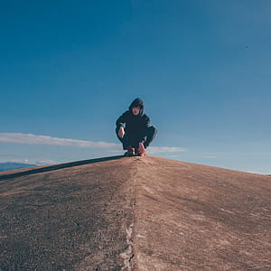 Man in Black Hoodie and Pants Sitting on Top of Rocky Cliff thumbnail