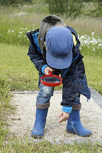 child wearing blue jacket, hat, and boots holding magnifying glass thumbnail