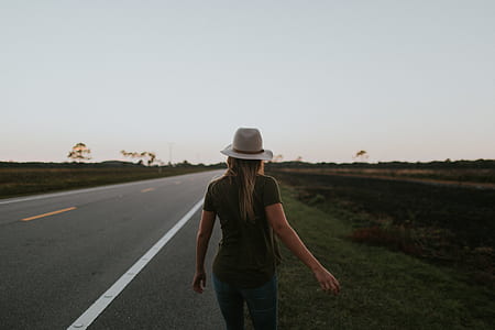 woman wearing green top and grey hat while walking on grey asphalt road during sunset thumbnail