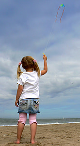 girl holding string of kite flying under white cloudy sky near seashore at daytime thumbnail