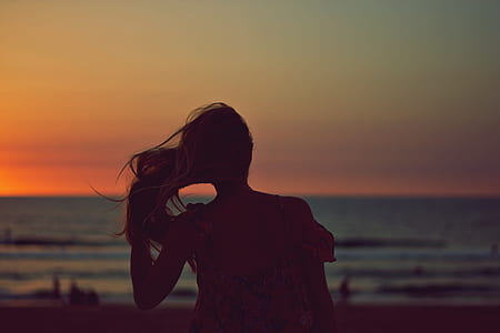 silhouette of woman holding her hair sitting on shore thumbnail