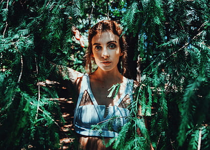 woman wearing blue sleeveless crop top standing between green plants thumbnail