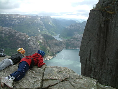 two boys prone lying on rock formation near body of water during daytime thumbnail