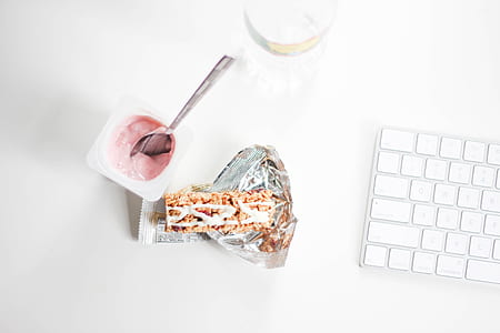 yogurt with stainless steel spoon near grey and white Magic Keyboard thumbnail