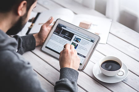 man wearing gray sweater using white tablet computer beside cup filled black coffee thumbnail