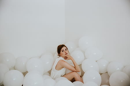 woman wearing sleeveless top sitting on the floor surrounded with white balloons thumbnail