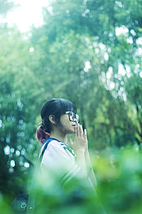 shallow focus photography of black haired girl wearing eyeglasses surrounded by green trees thumbnail