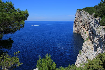 rocky mountain cliff beside beach under blue skies daytime thumbnail