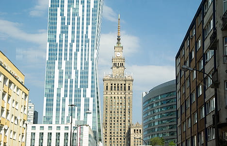 gray concrete tower building with analog clock between white and brown buildings at daytime thumbnail