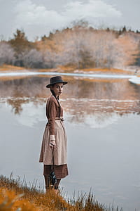 woman standing on brown grass carrying black camera in front lake at daytime thumbnail