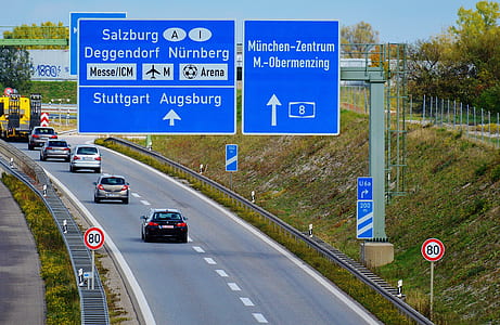 blue and white road signage near vehicles on black concrete road at daytime thumbnail