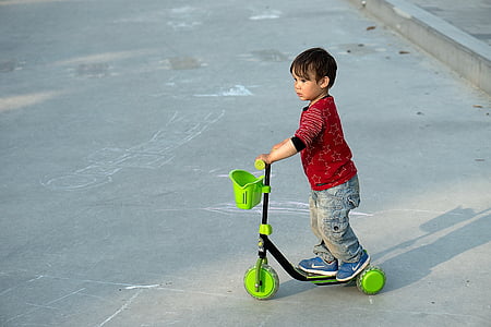 boy riding black and green 3-wheeled kick scooter thumbnail