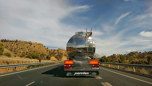 white car reflected on tank truck on highway between trees thumbnail