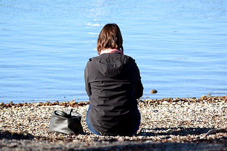 woman sitting on gray sand seashore wearing black hooded jacket thumbnail