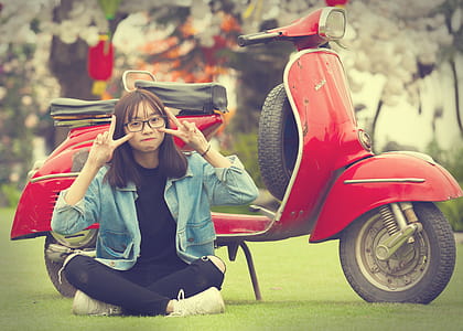 Girl Doing Peace Sign Indian Sitting in Front of Red Scooter Motorcycle thumbnail