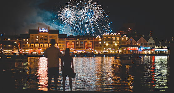 man and woman standing near body of water watching fireworks thumbnail