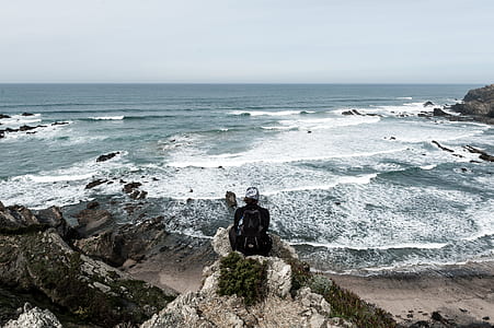 person sitting on rock cliff surrounded with water thumbnail