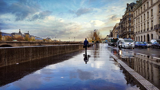 person walking on wet floor beside brown concrete wall and parked vehicles at daytime thumbnail