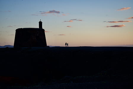 silhouette photography of two person sanding beside lighthouse during sunset thumbnail