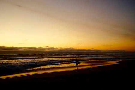 silhouette of person on beach shore during orange sunset thumbnail