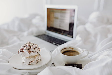 Woman working on a laptop while enjoying a breakfast coffee and chocolate in bed thumbnail