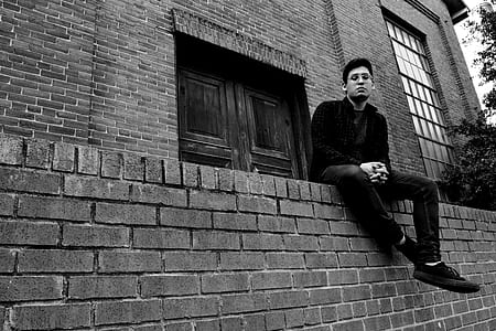 Grayscale Photography of Man Sitting on Brick Fence thumbnail