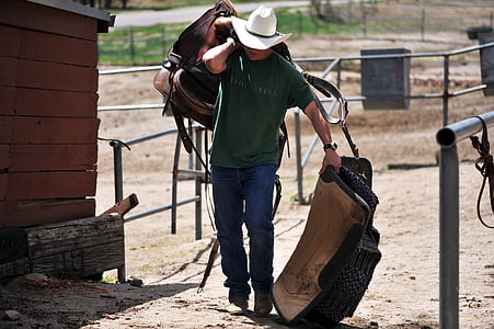 man in green crew-neck shirt holding brown horse saddle thumbnail