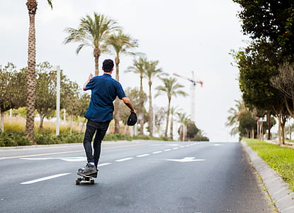 man stands on skateboard on road between trees at daytime thumbnail