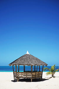 black and brown wooden nipa house in front of body of water thumbnail